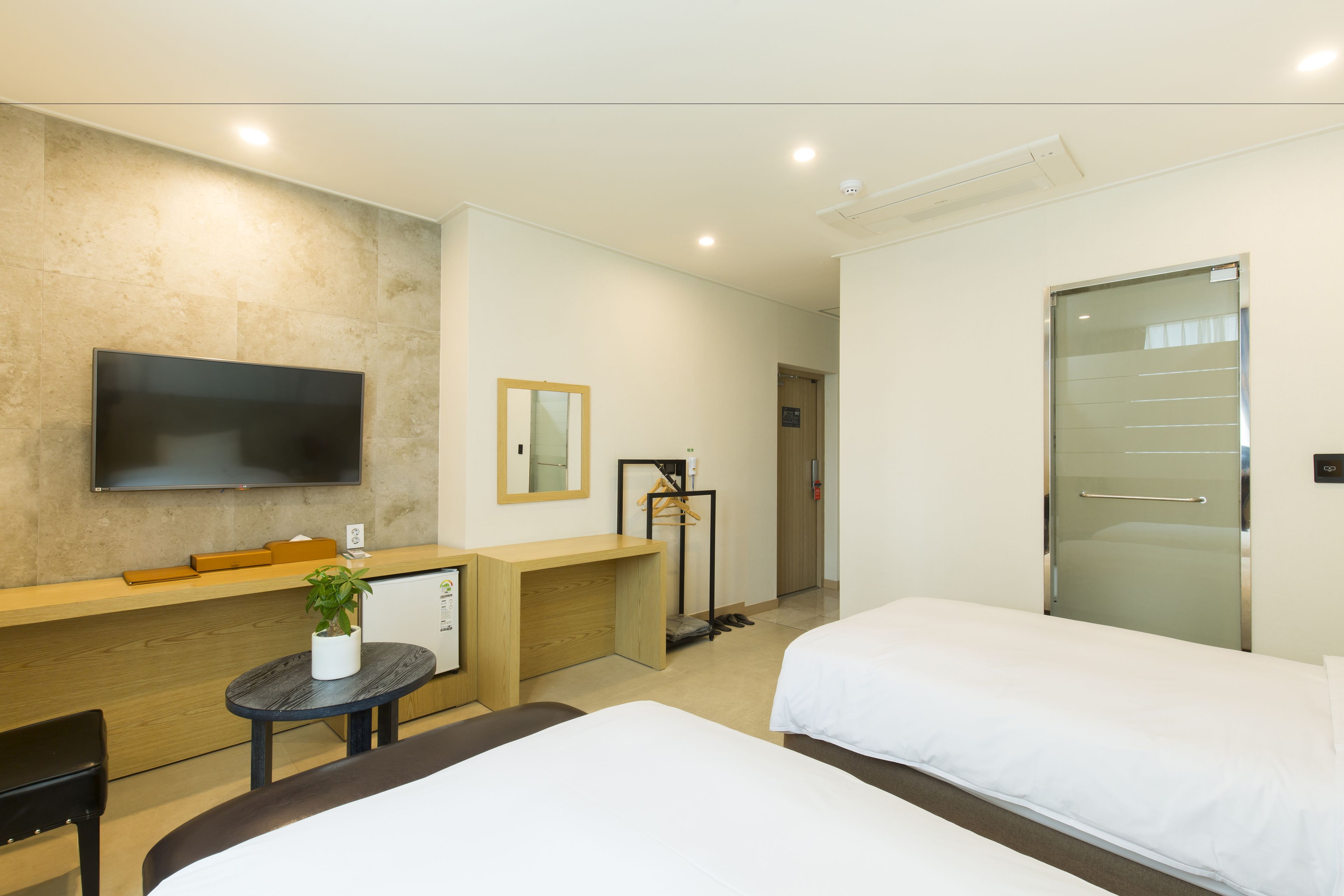 Habitación de hotel con dos camas, un televisor montado en la pared, un escritorio con una silla y una mesita con una planta.