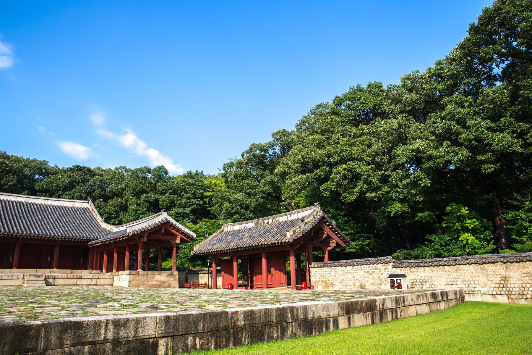 A traditional Korean pavilion with a tiled roof, surrounded by a stone wall and lush greenery.