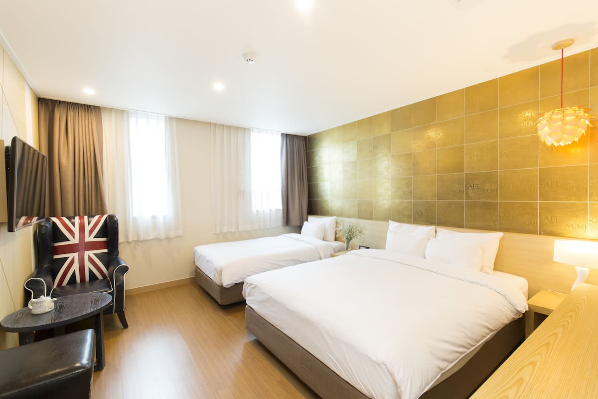 A hotel room with two beds, a small table, a chair with a Union Jack cushion, and a wall-mounted TV.