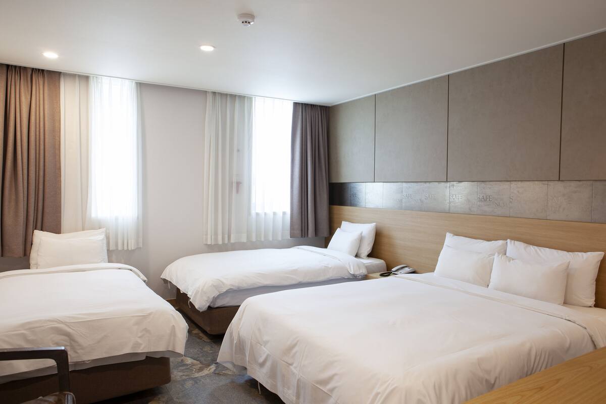 A hotel room with three single beds, a wooden headboard, a desk, and a chair.