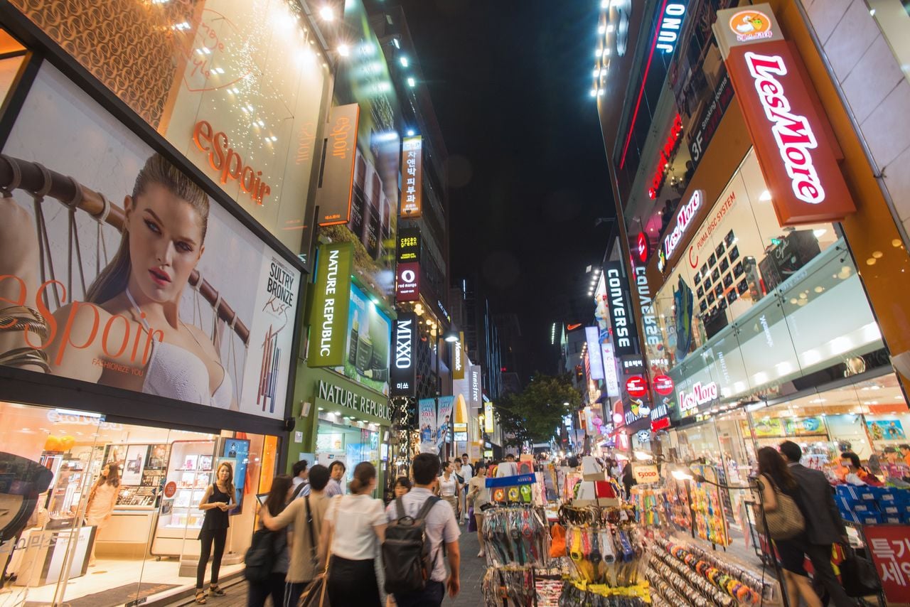 A busy urban street at night with illuminated storefronts and pedestrians.