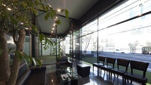 A modern indoor seating area with glass walls, a tree, and a view of the street. - Hotel Nafore (Seoul)