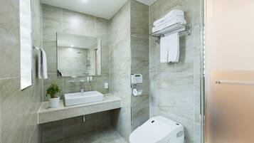 A modern bathroom with a marble sink, a toilet, a glass shower enclosure, and a towel rack with folded towels.