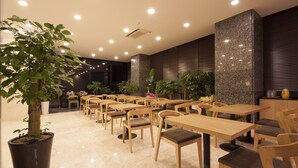 A modern indoor dining area with wooden tables and chairs, potted plants, and recessed ceiling lighting. - Hotel Nafore (Seoul)