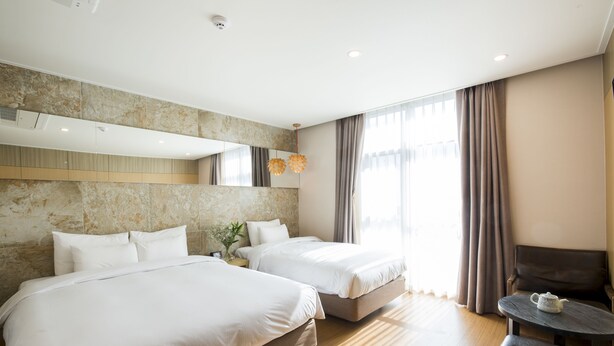 A hotel room with two beds, a small table, a sofa, and a large window with curtains. - Hotel Nafore (Seoul)