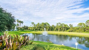 A golf course with a pond, lush greenery, and a fountain.