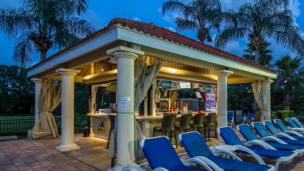 A covered outdoor seating area with blue lounge chairs and a bar.