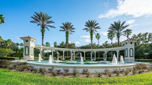 A fountain with multiple water jets, surrounded by palm trees and a clear blue sky.