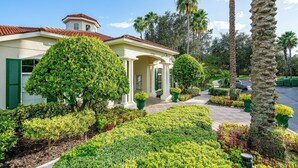 A two-story house with a red-tiled roof, a covered porch with columns, and a well-maintained garden with various shrubs and palm trees.
