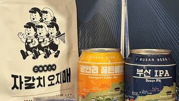 A variety of Korean food and beverages, including a bag of snacks, a can of Gwanganni Golden Ale, a can of Busan IPA, and a box of Busan Caramel.