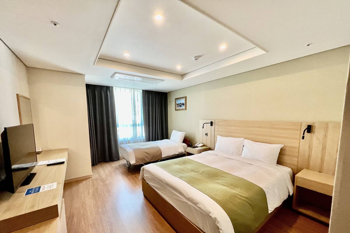 A hotel room with two beds, a desk with a computer, a TV, and a window with curtains.