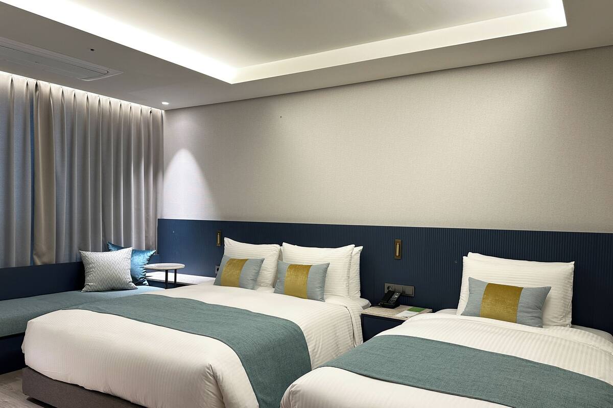 A hotel room with two beds, a bedside table, a lamp, and a window with curtains.
