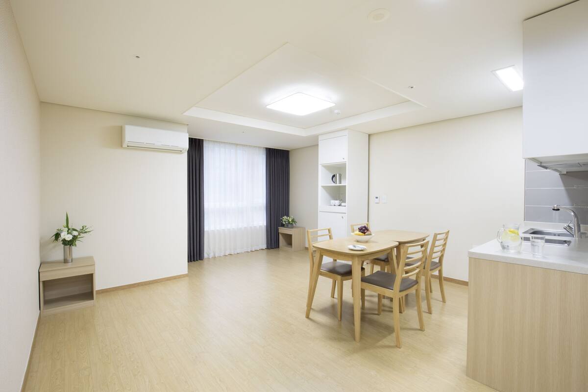 A modern, well-lit room with a dining table, chairs, a small kitchen area, and a built-in shelf.
