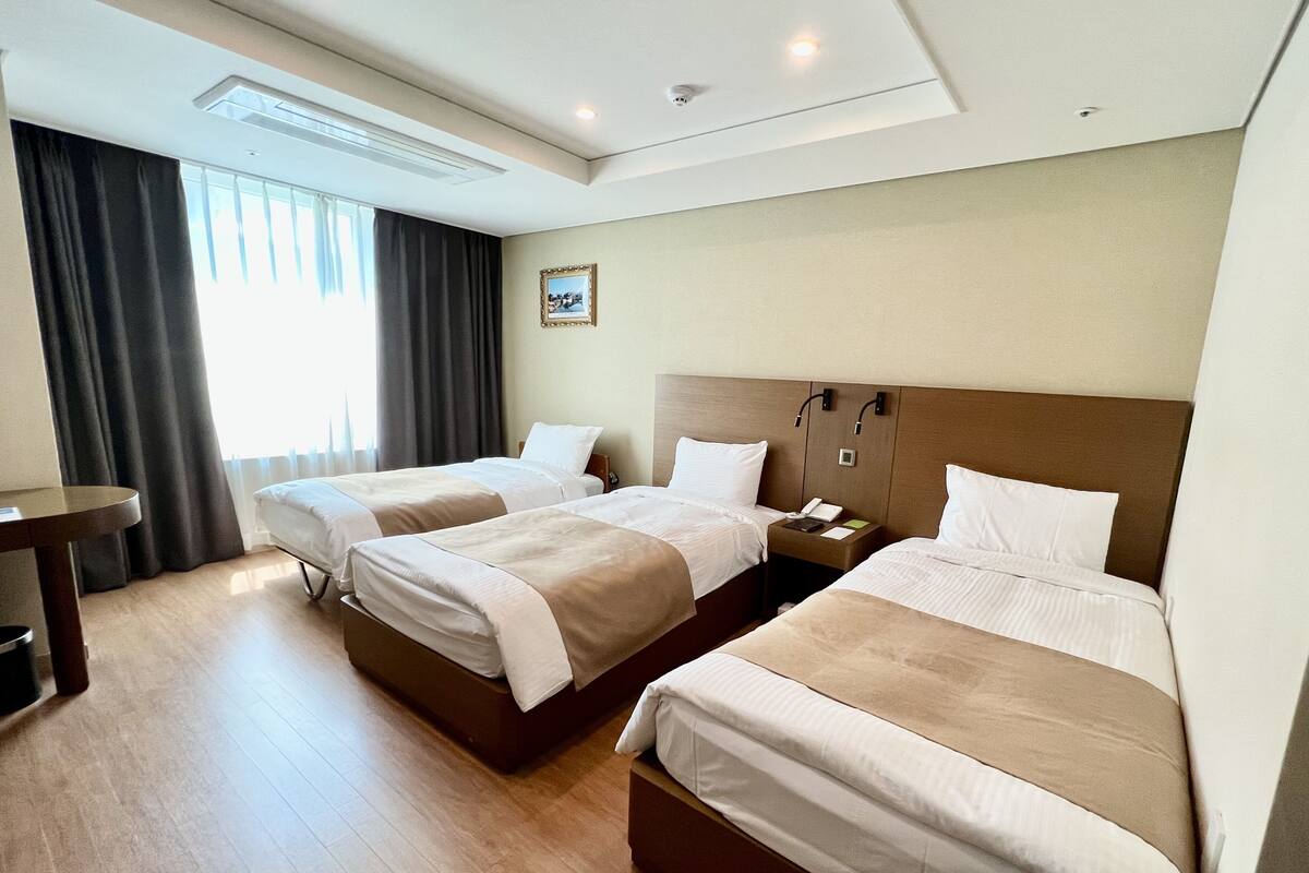 A hotel room with two beds, a bedside table, a desk, and a window with curtains.