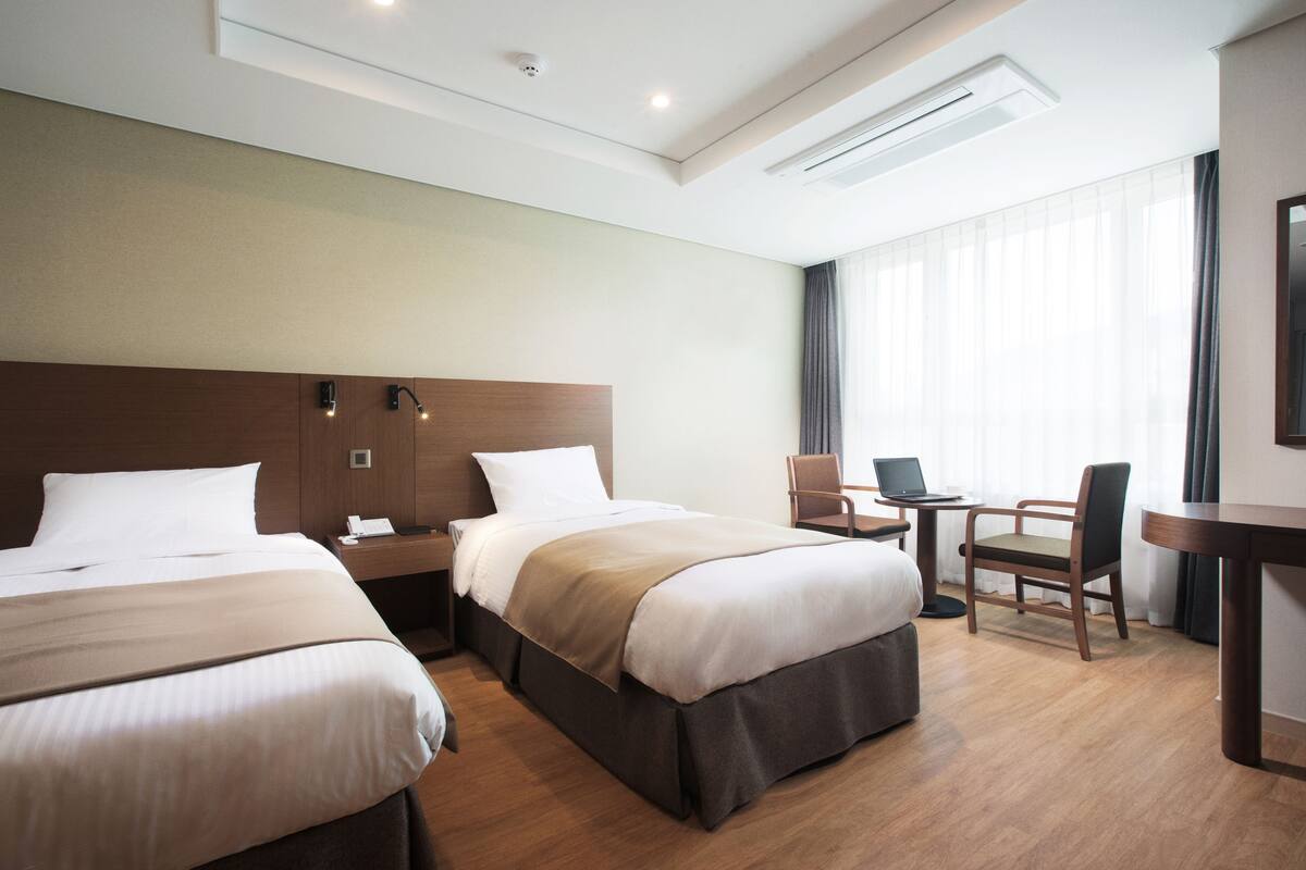 A hotel room with two beds, a desk, a chair, and a laptop.