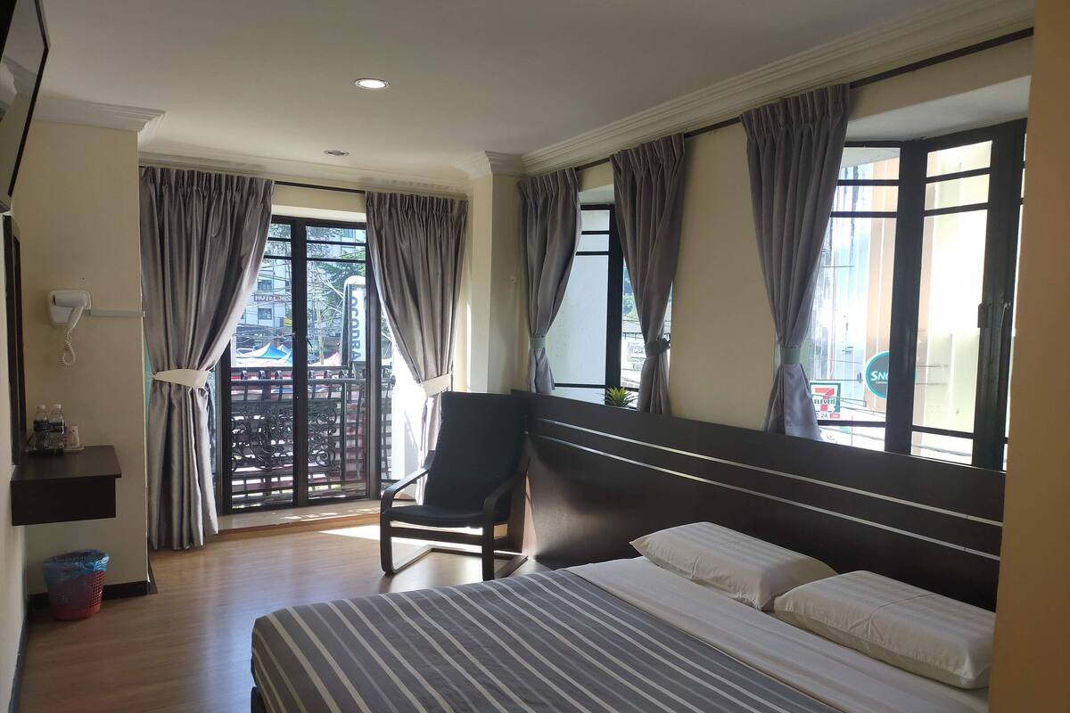 Une chambre d’hôtel avec un lit, une chaise, un bureau avec un téléphone et une fenêtre avec des rideaux.