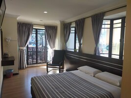 Una camera d'albergo con un letto, una sedia, una scrivania con il telefono e una finestra con tende.