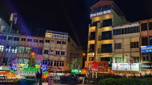 Un hotel con varios pisos, un letrero que dice 'Hong Kong Hotel' y un edificio cercano con la señalización 'Persatuan Hanggam Cameron Highlands'.
