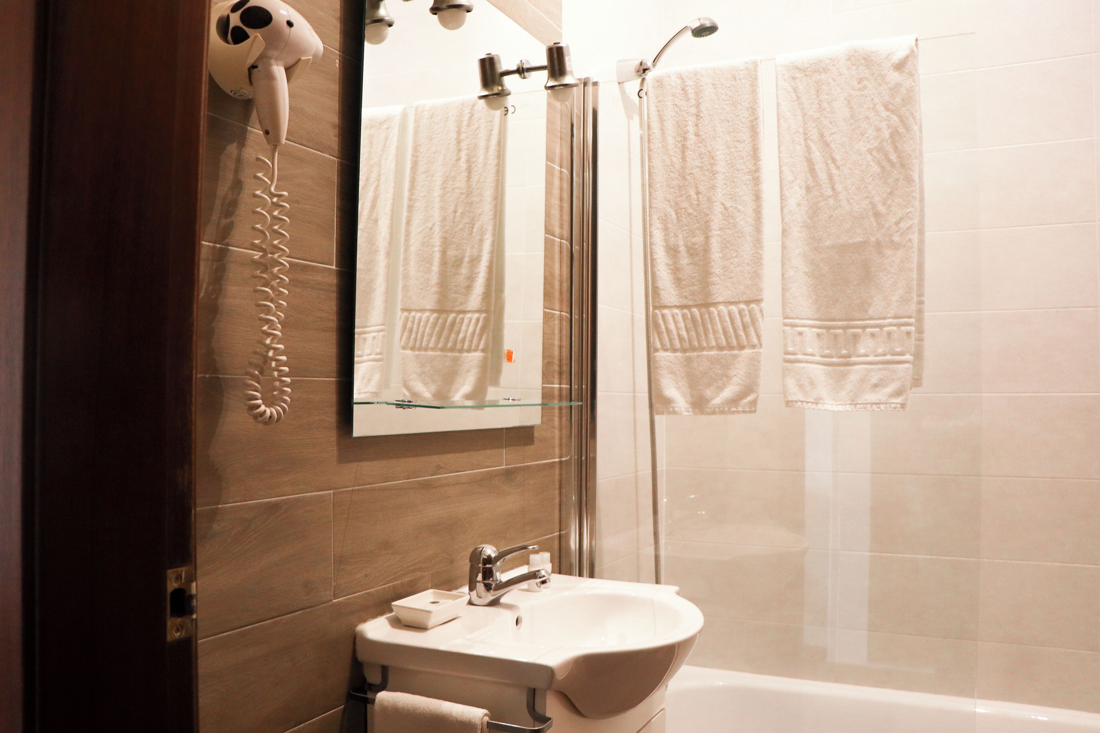 A bathroom with a glass shower enclosure, a sink with a mirror above it, and two towels hanging on the wall.