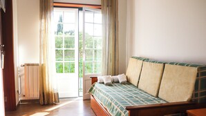 A bedroom with a wooden bed, a window with curtains, and a view of greenery outside. - Hotel Louro (Obidos)