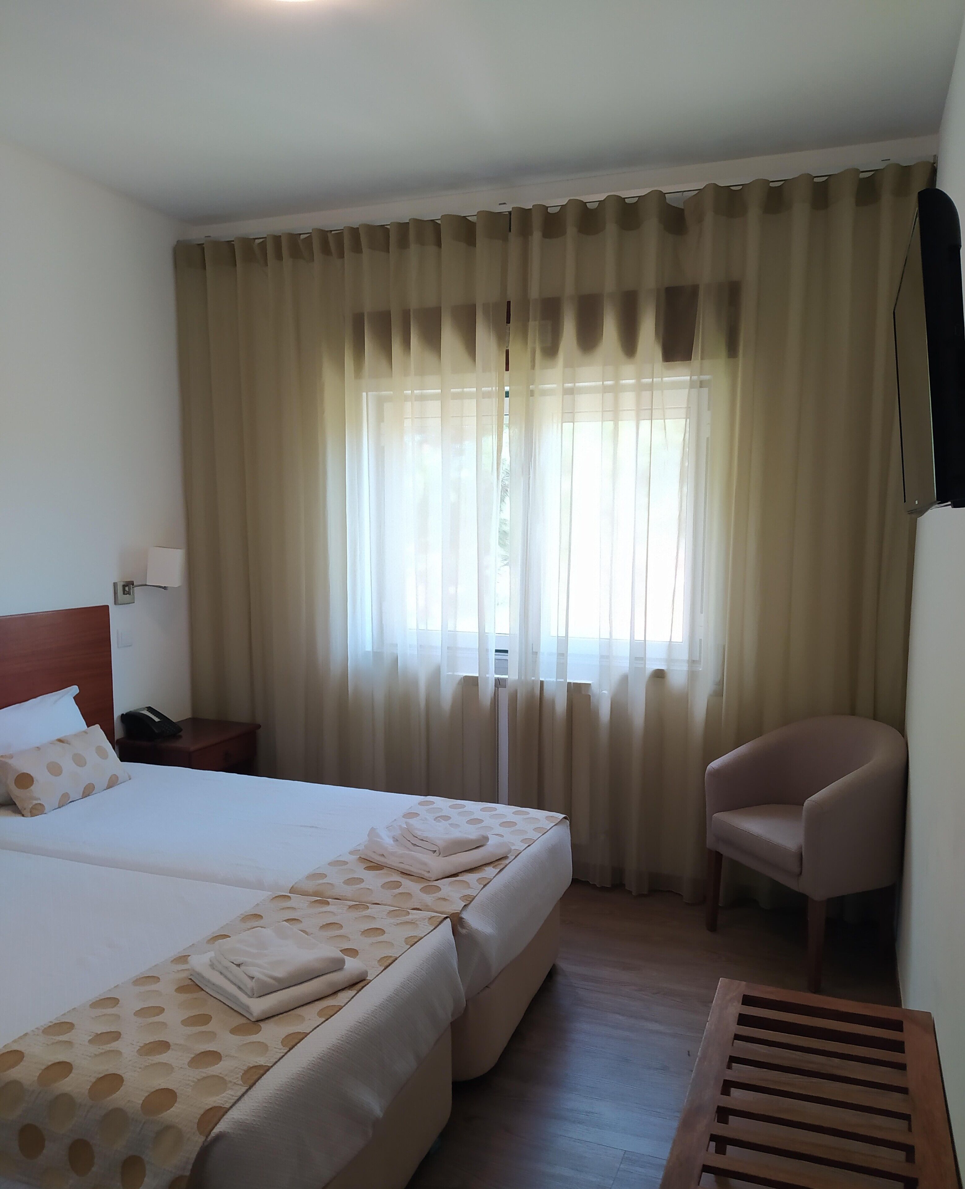 Habitación de hotel con una cama grande, una silla, una mesita de noche con lámpara y una ventana con cortinas.