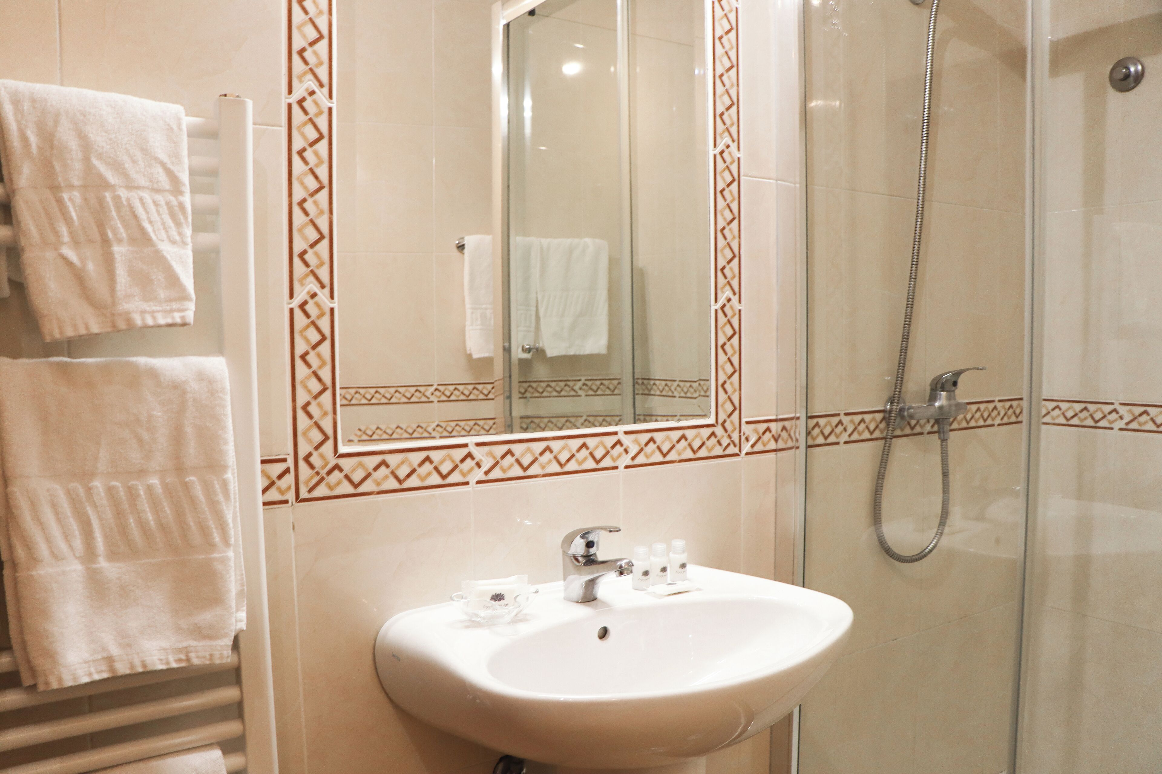 A bathroom with a white sink, a glass shower enclosure, and a mirror with a decorative border.