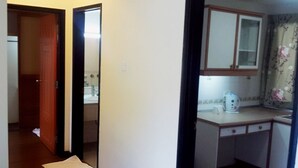 A narrow hallway leading to a kitchen with a wooden door, a white countertop, and a window with a floral curtain. - E Resort (Brinchang)