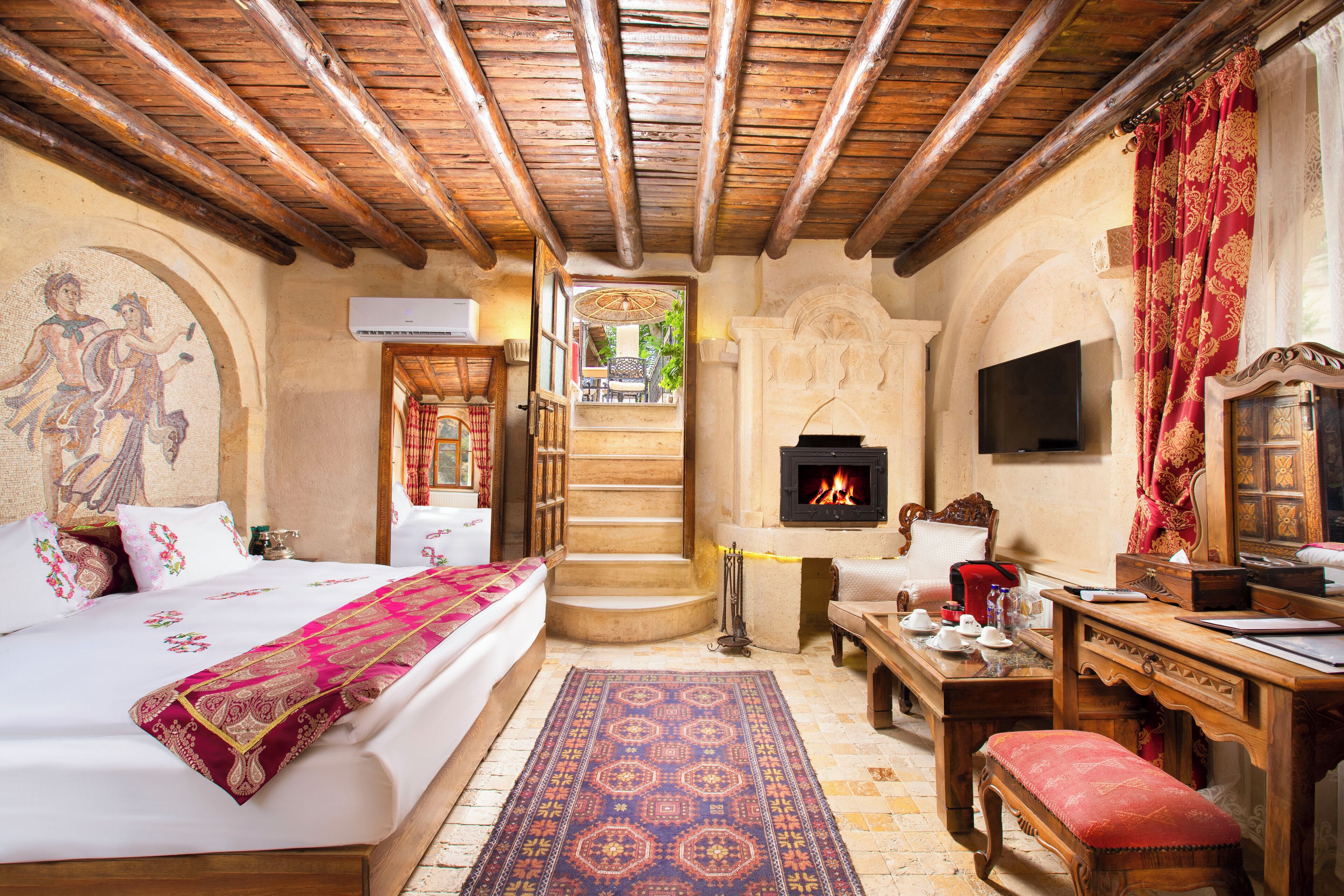 A traditional room with a bed, a wooden desk, a fireplace, and a view of the outside.