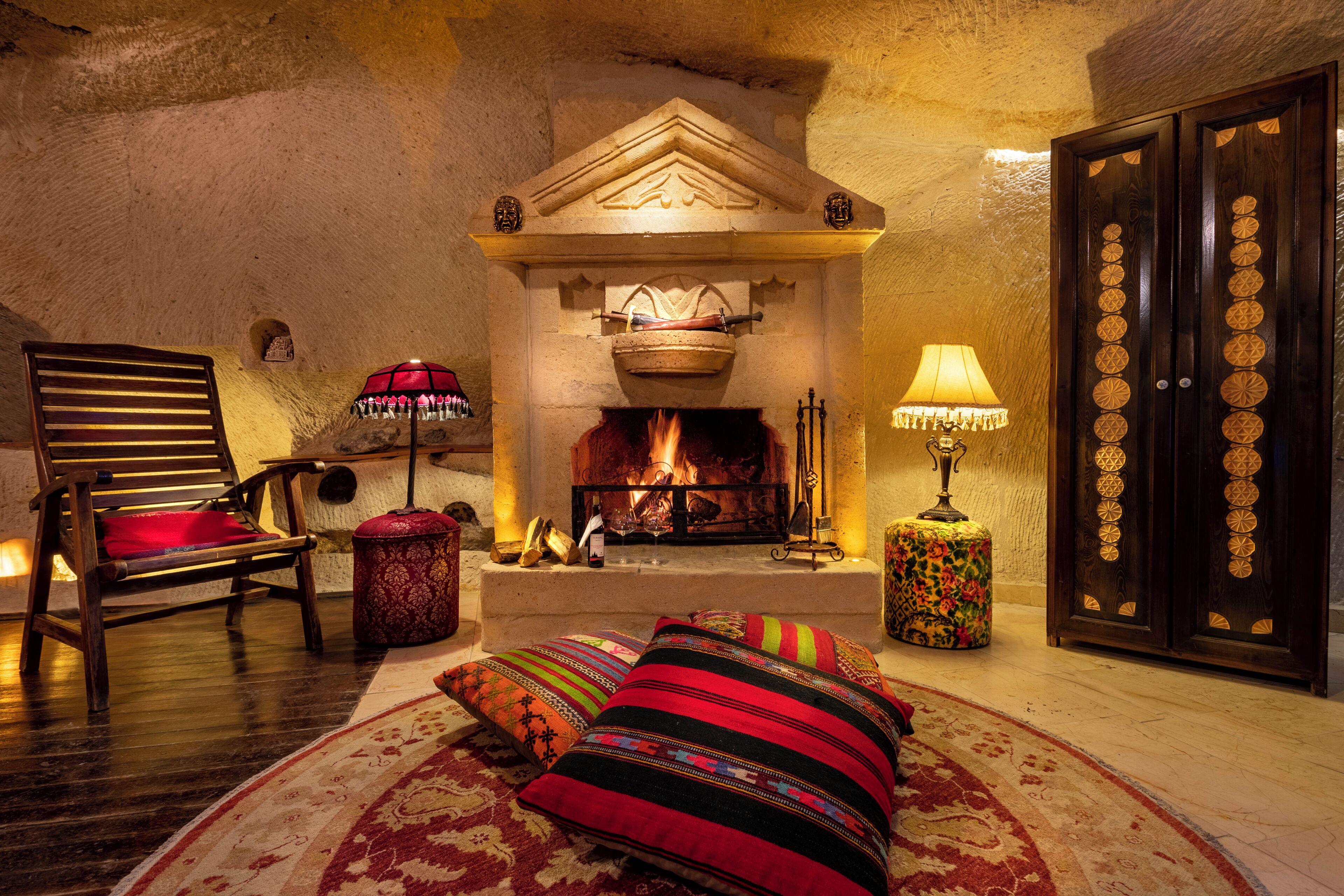 A cozy room with a fireplace, a wooden chair, a patterned rug, and a decorative lamp.
