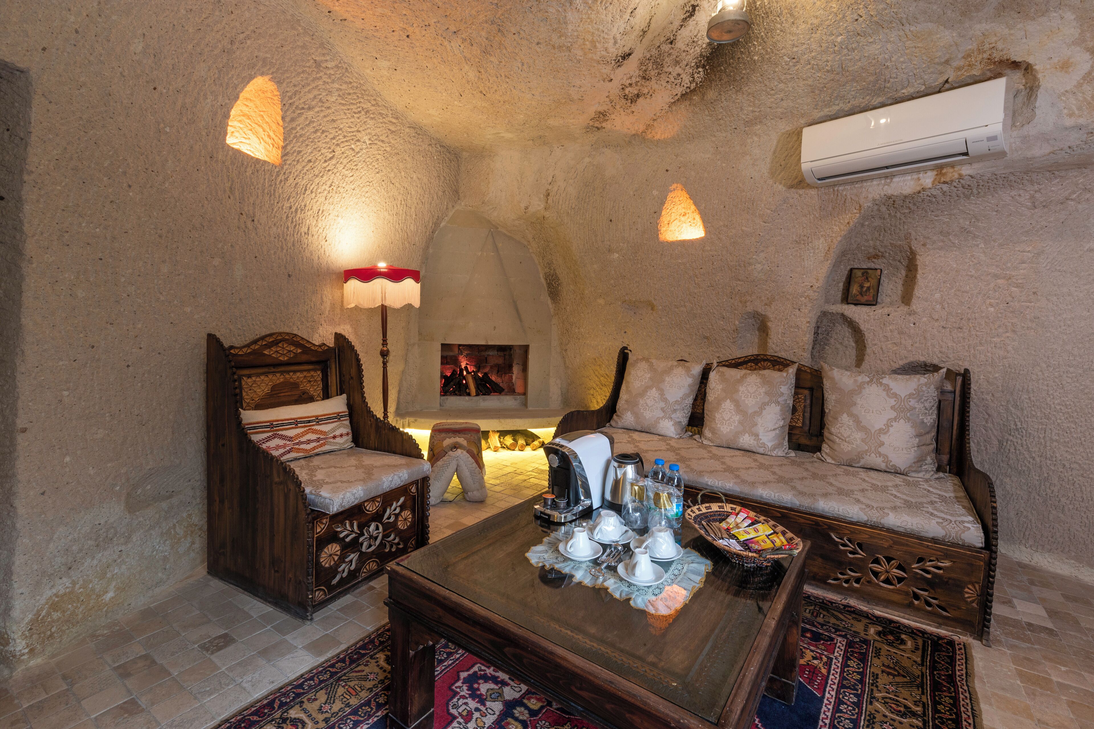 Un interior acogedor con pared de piedra, chimenea, sofá, mesa de centro de madera y alfombra estampada.