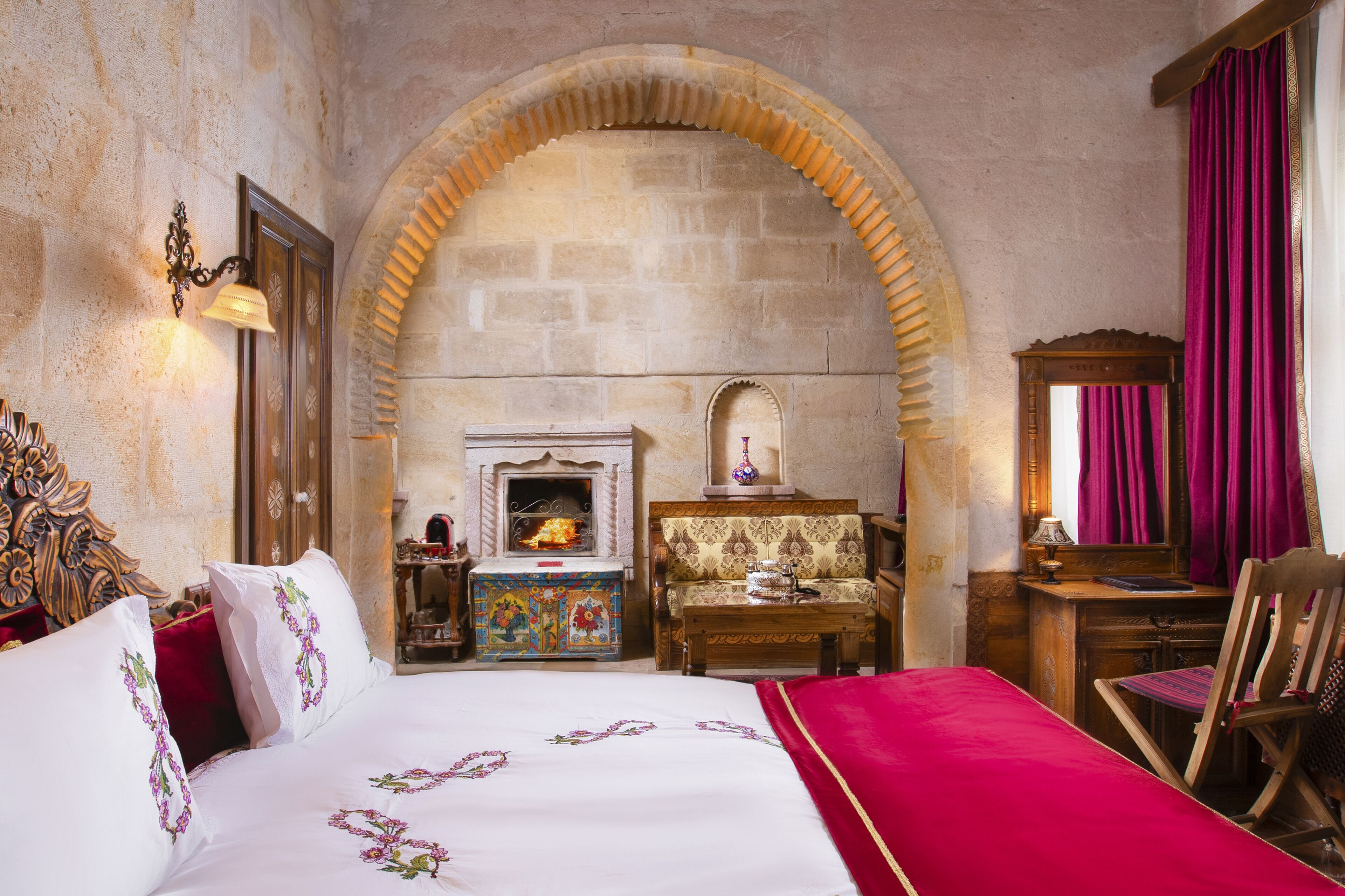 A historic room with a stone archway, a bed with embroidered linens, a fireplace, and traditional furnishings.