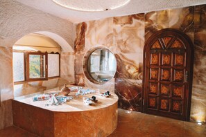 A marble bathroom with a round mirror, a wooden door with intricate patterns, and a bench.