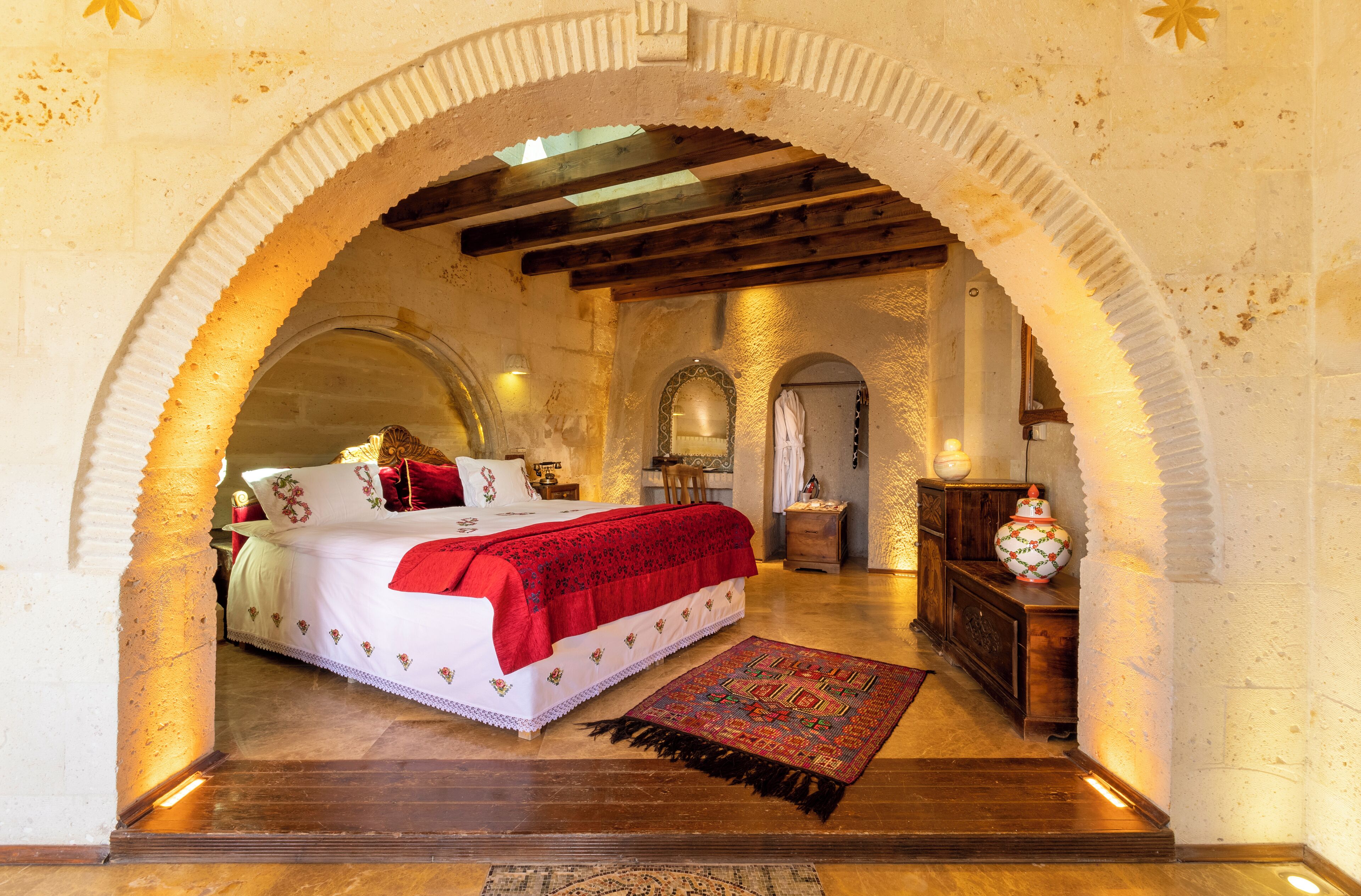 A bedroom with a large bed, a wooden floor, and an arched doorway.