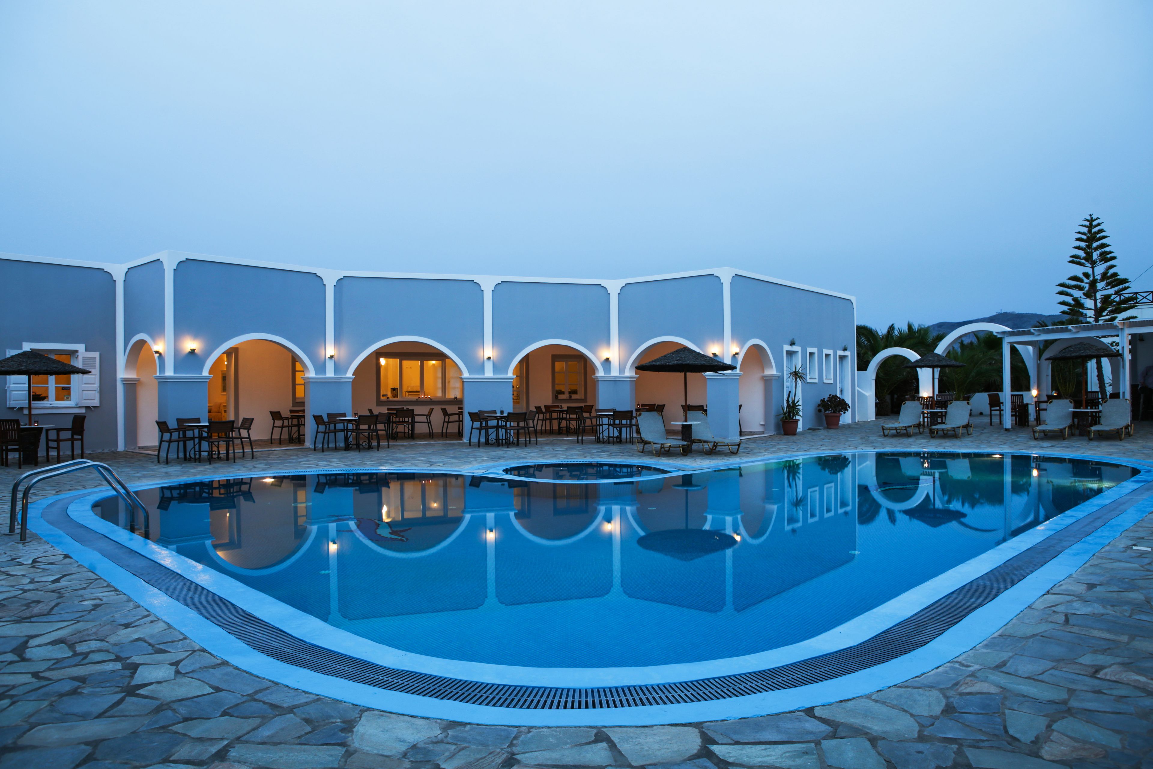 Una piscina con baldosas de piedra, rodeada de mobiliario de exterior y un edificio con arcos.