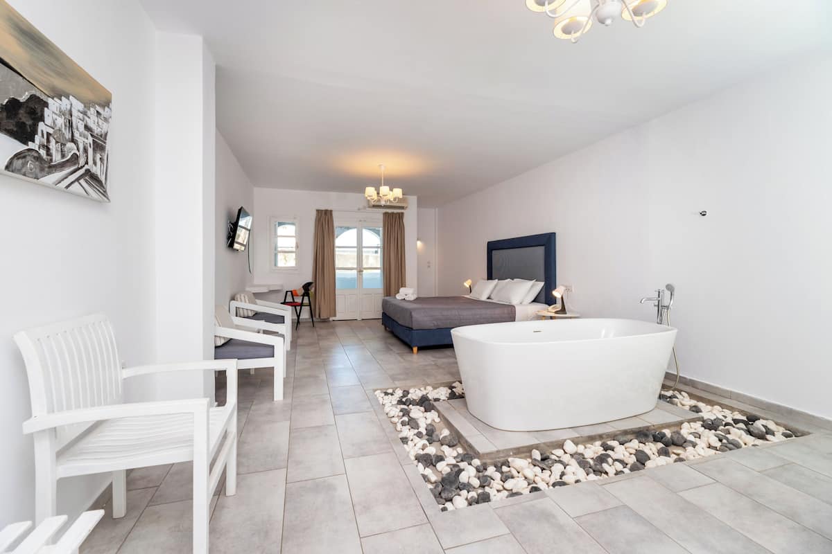 A modern bedroom with a large bed, a white bathtub, and a seating area with a white chair and sofa.