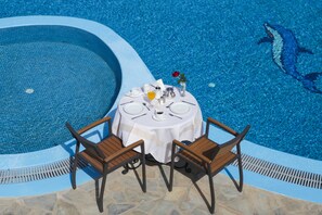A round table with four chairs by a pool with a dolphin mosaic. - Maistros Village (Santorini)