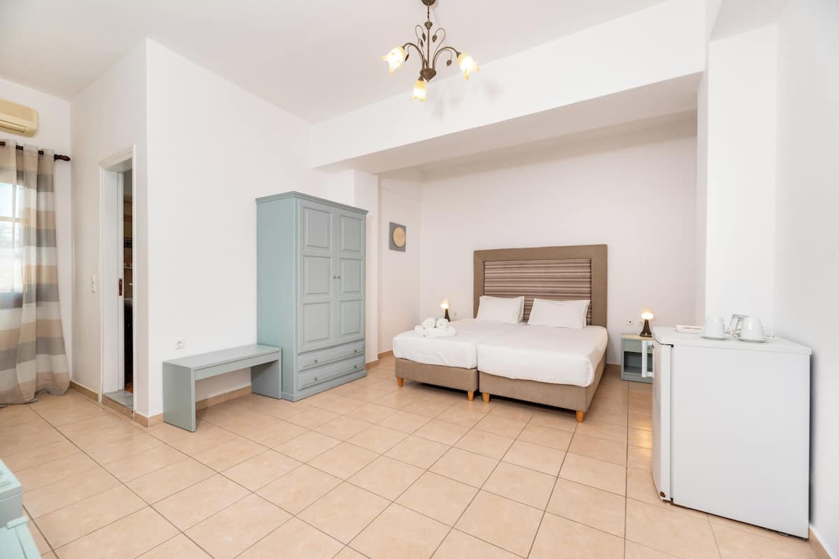 A bedroom with a bed, a bench, a wardrobe, a nightstand, and a refrigerator.