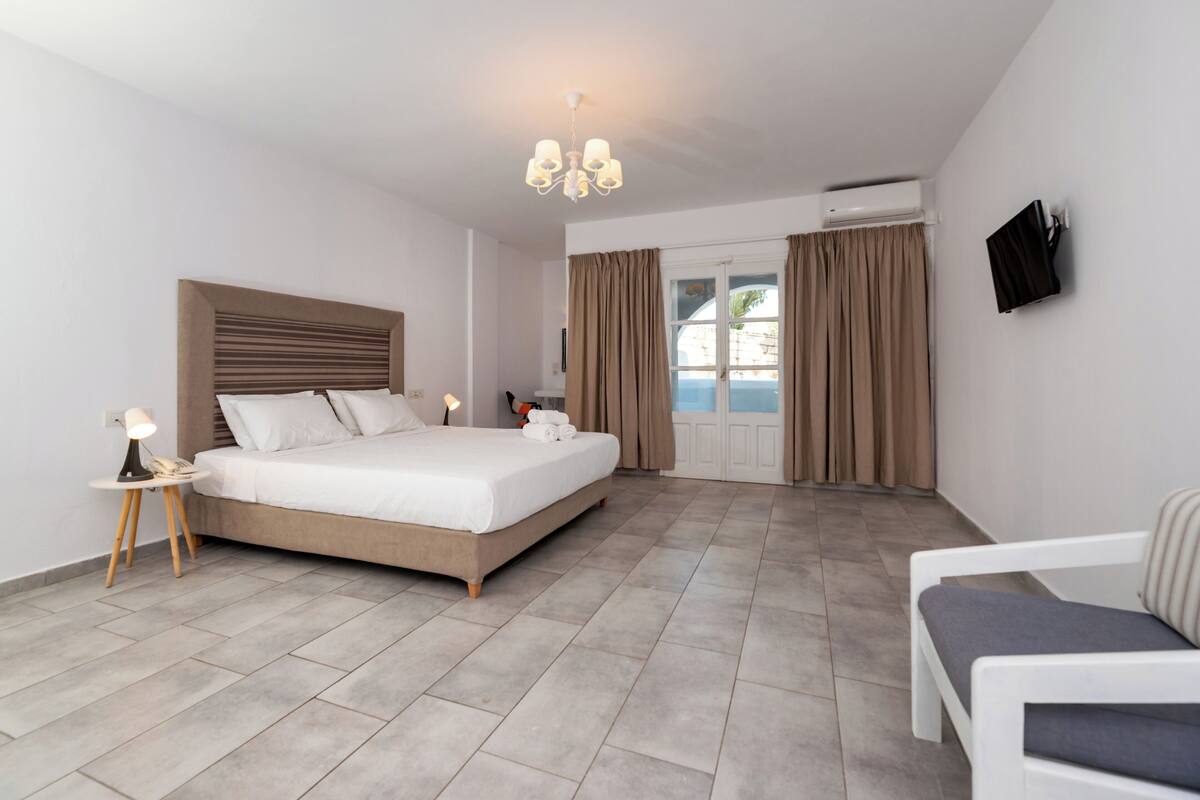 A hotel room with a bed, bedside table, lamp, chair, and a TV mounted on the wall.