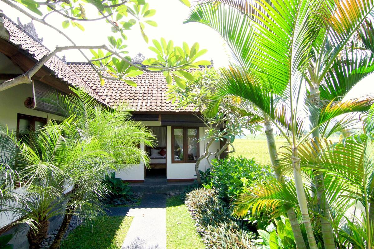 A house with a tiled roof, surrounded by lush greenery and palm trees.
