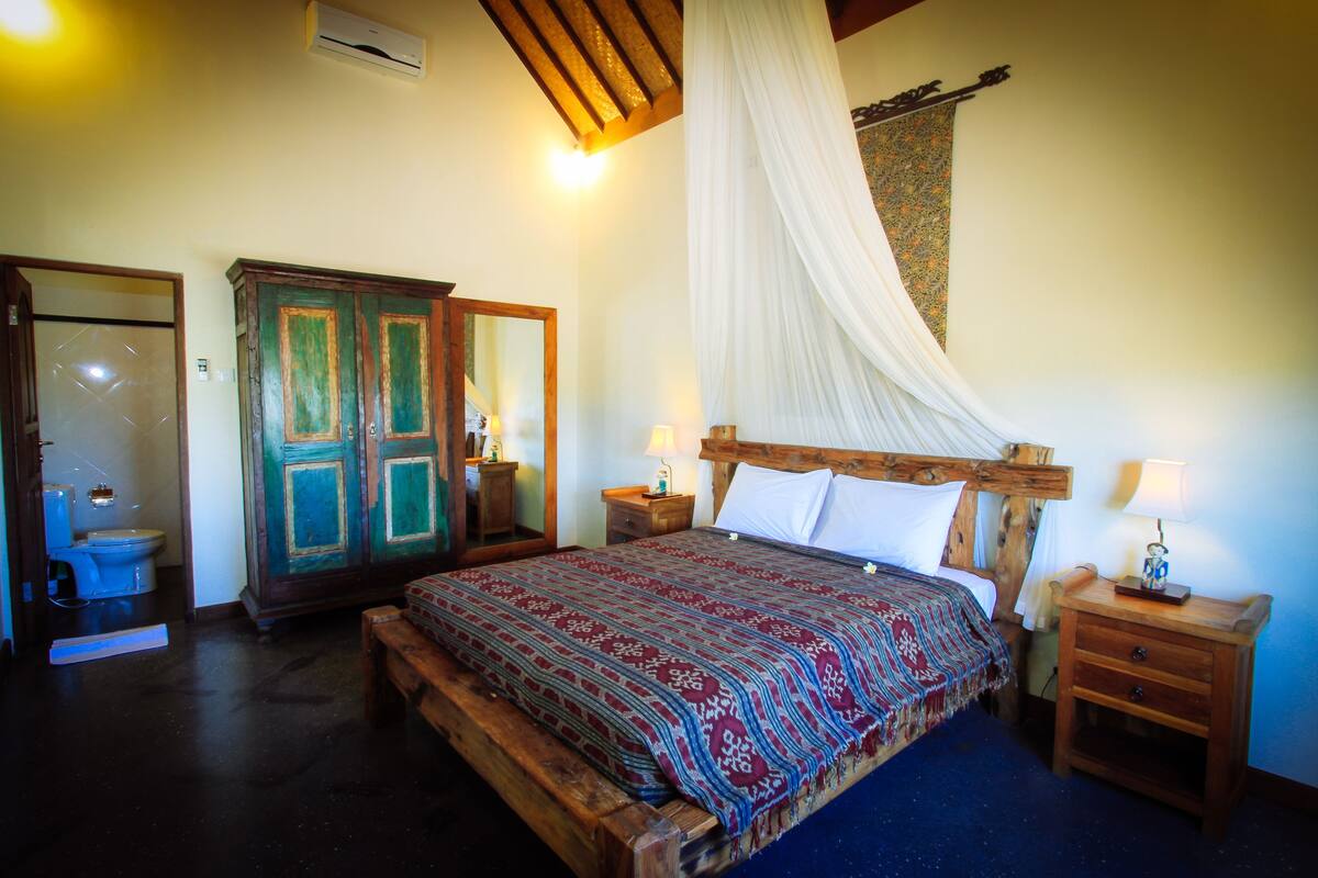 A bedroom with a wooden bed, a nightstand, a bedside table, a mirror, a wardrobe, and a bathroom with a toilet.