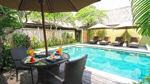 Un área junto a la piscina con una mesa y sillas, una piscina y sillones de descanso bajo sombrillas.