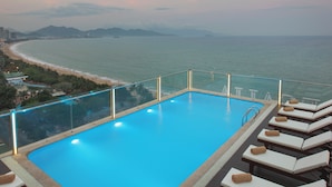 Piscina infinita no terraço com espreguiçadeiras e vista para a costa.