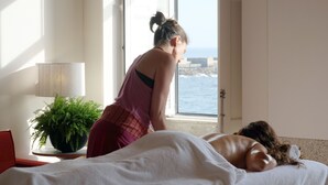 Ein Zimmer mit Bett, einer Topfpflanze und Meerblick durch ein offenes Fenster.