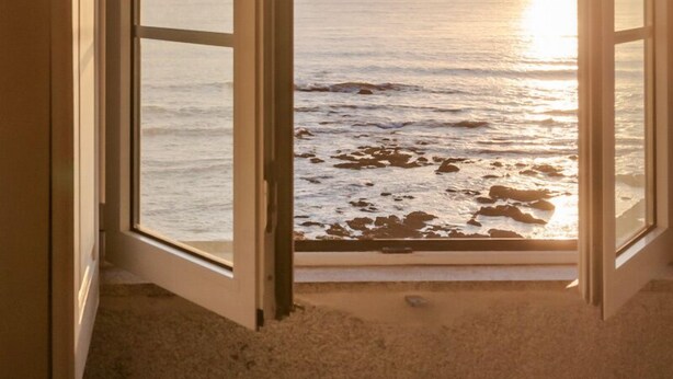 Ein offenes Fenster mit Blick auf den Ozean bei Sonnenuntergang.