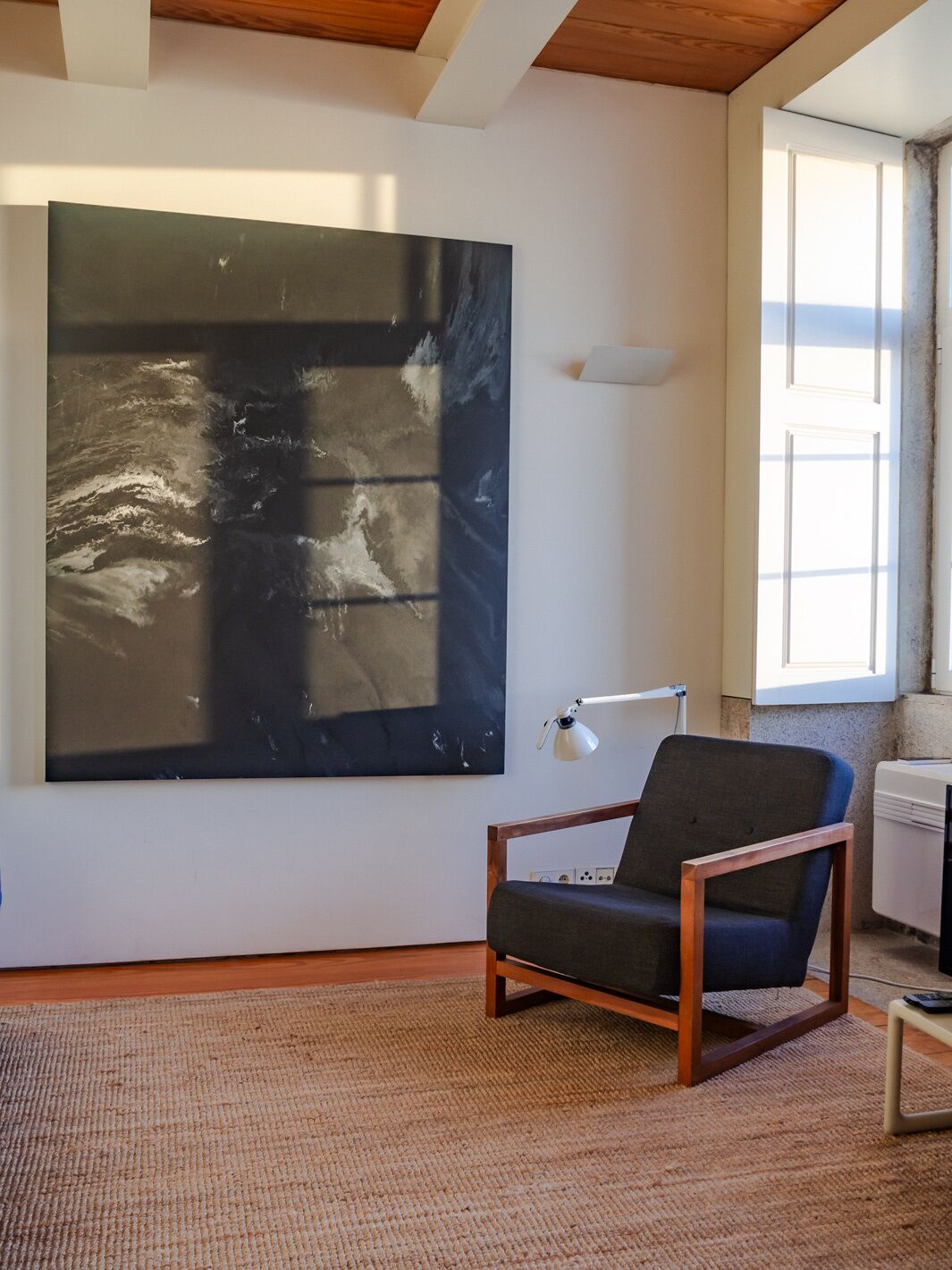 A modern living room with a large abstract painting, a wooden-framed chair, and a floor lamp.
