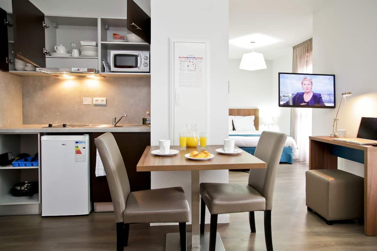 A modern hotel room with a kitchenette, a dining area with breakfast items, a TV, and a bed.