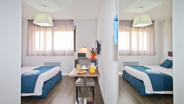 A hotel room with two beds, a dining table with breakfast items, and a TV.