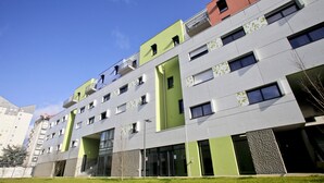 A modern multi-story building with a flat roof, large windows, and a green accent wall.