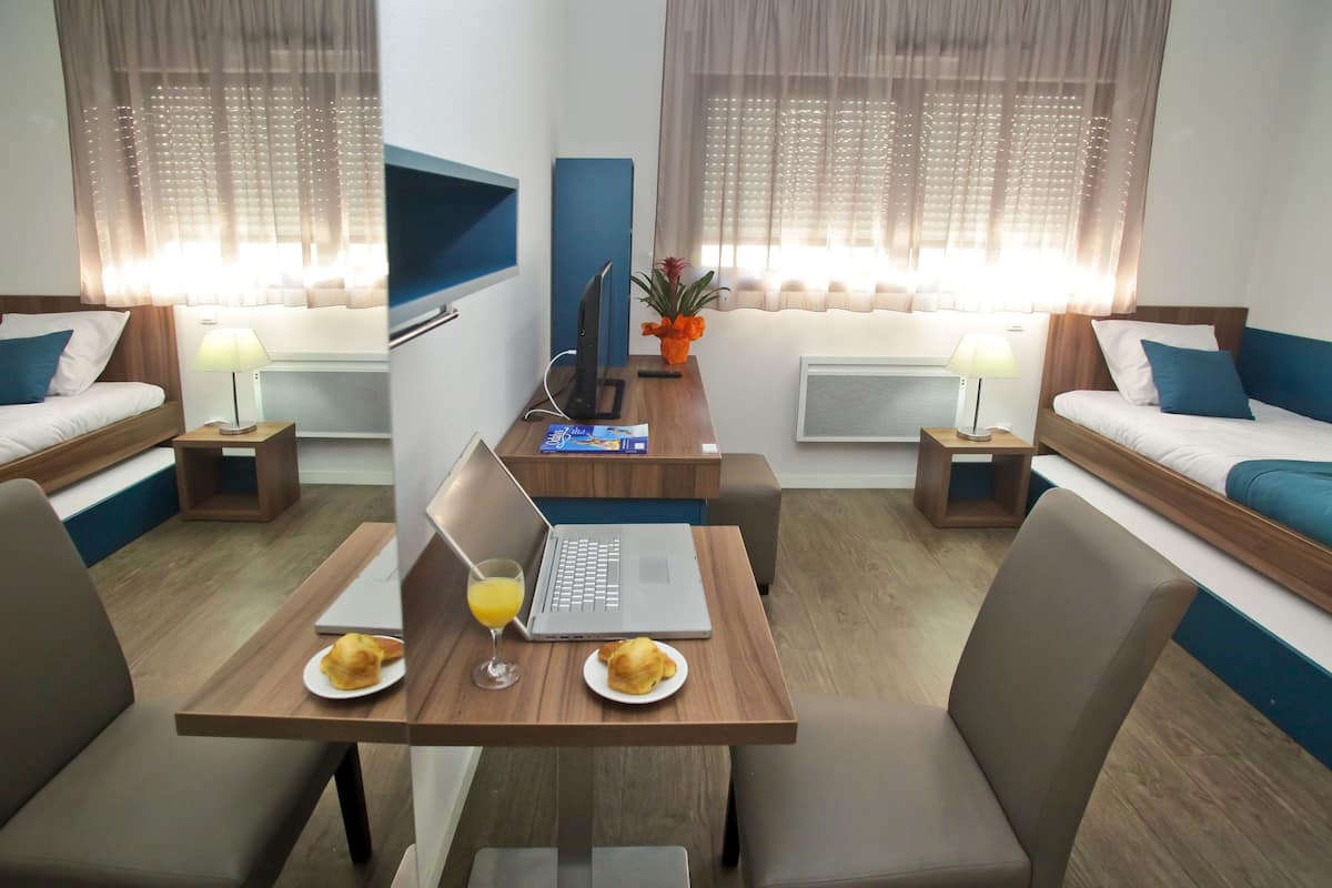 A hotel room with two beds, a desk with a laptop and breakfast, and a TV on the wall.