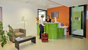 A reception area with a green counter, a beige sofa, a coffee table, and a red suitcase.